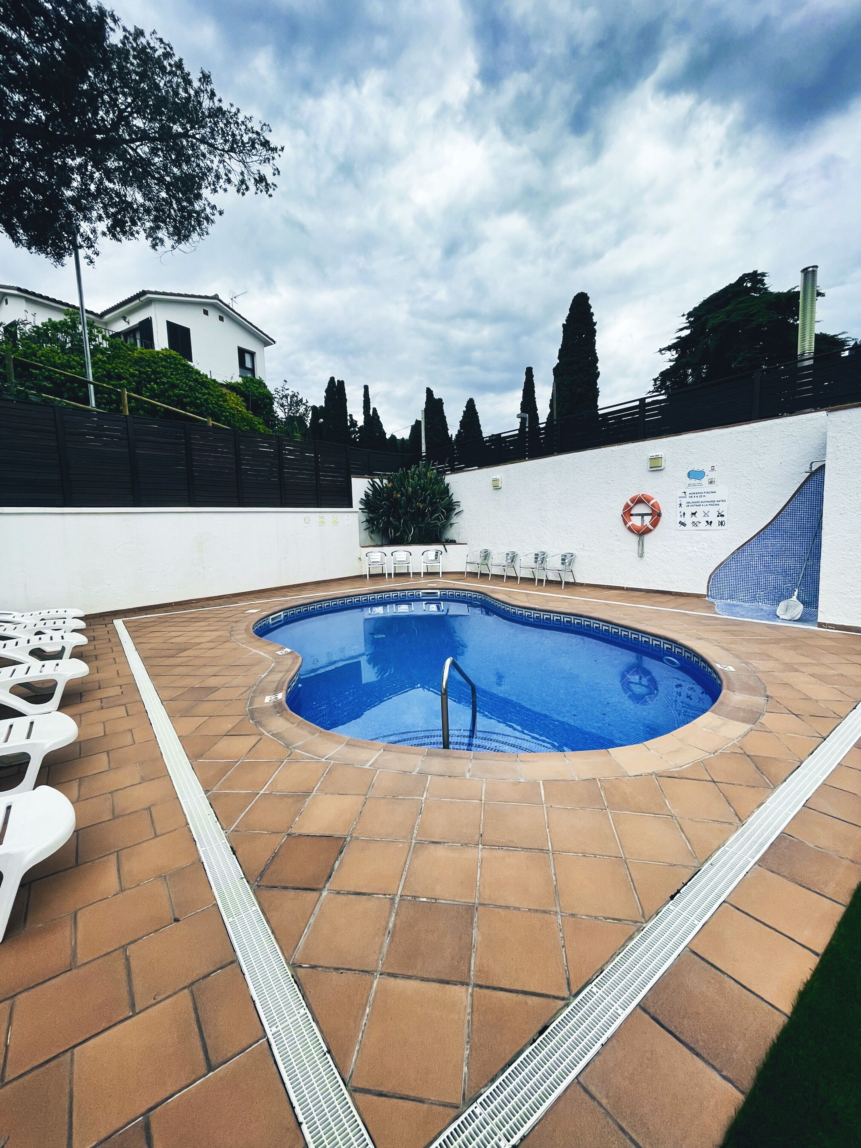 A swimming pool with a tiled deck, surrounded by a white wall and a black fence.