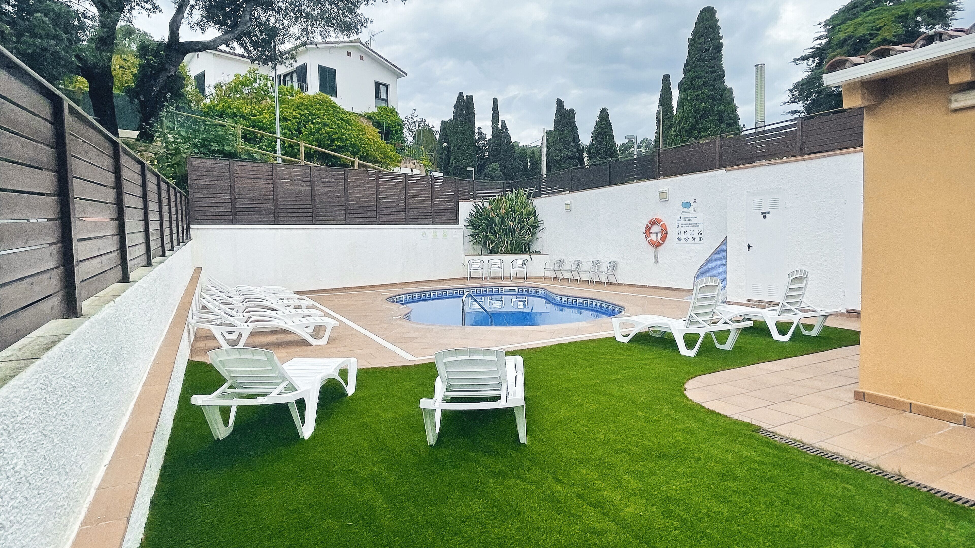A swimming pool surrounded by white lounge chairs and a grassy area.