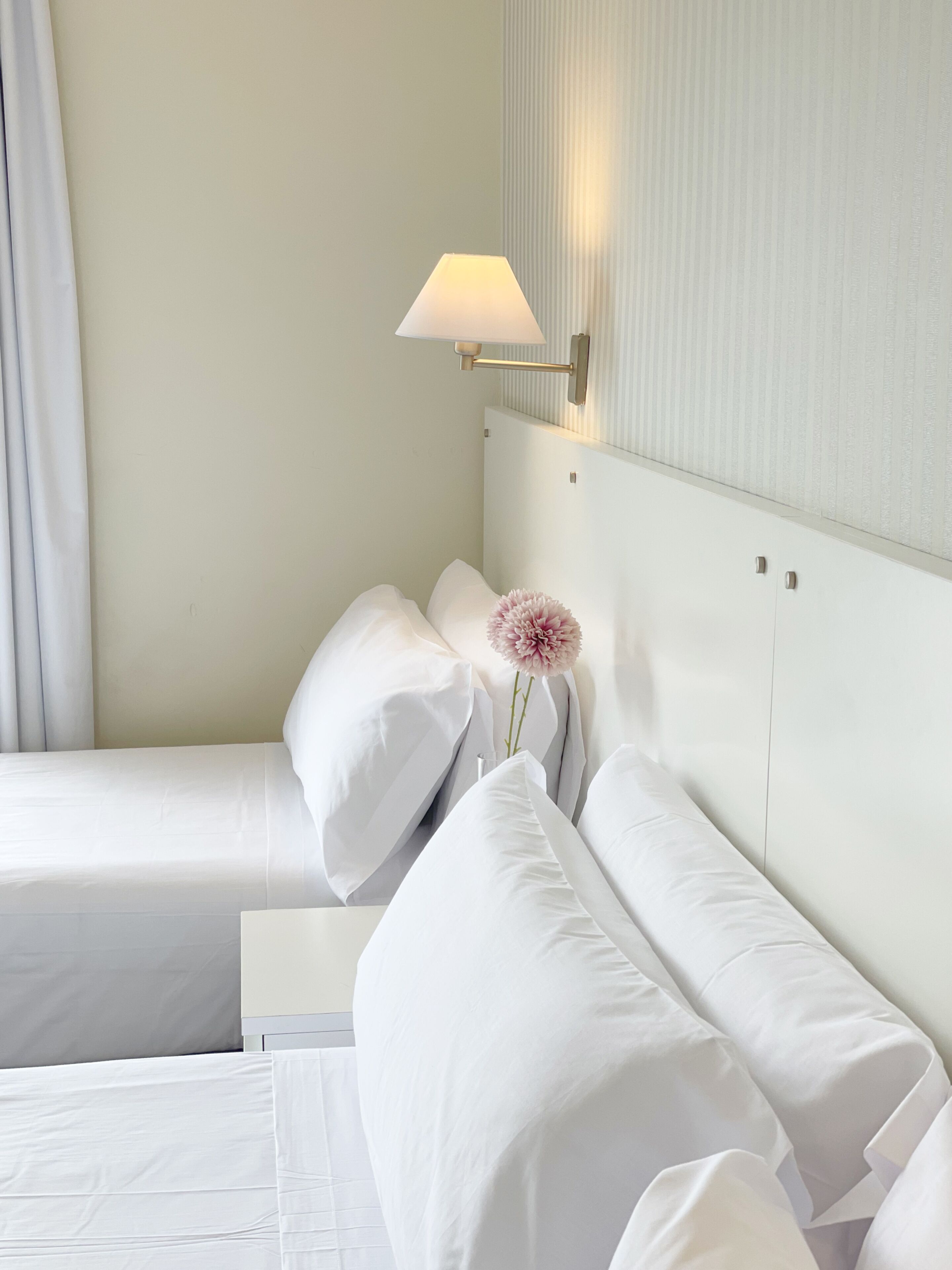 Habitación de hotel con dos camas, una mesita de noche, una lámpara y un jarrón con una flor.