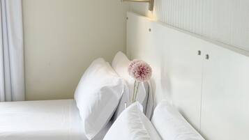 Habitación de hotel con dos camas, una mesita de noche, una lámpara y un jarrón con una flor.