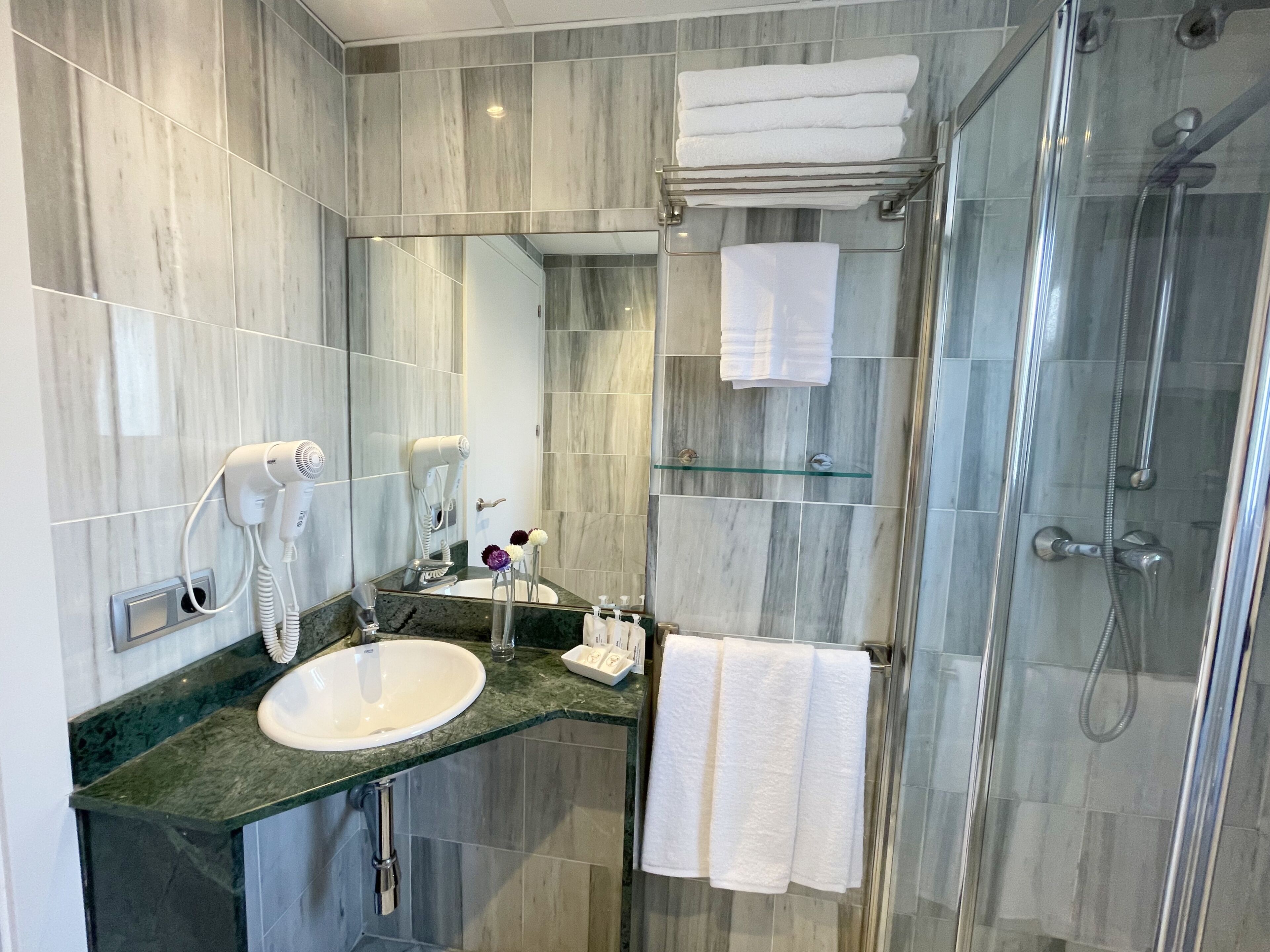 A modern bathroom with a marble sink, a glass shower enclosure, and a vanity with a mirror.