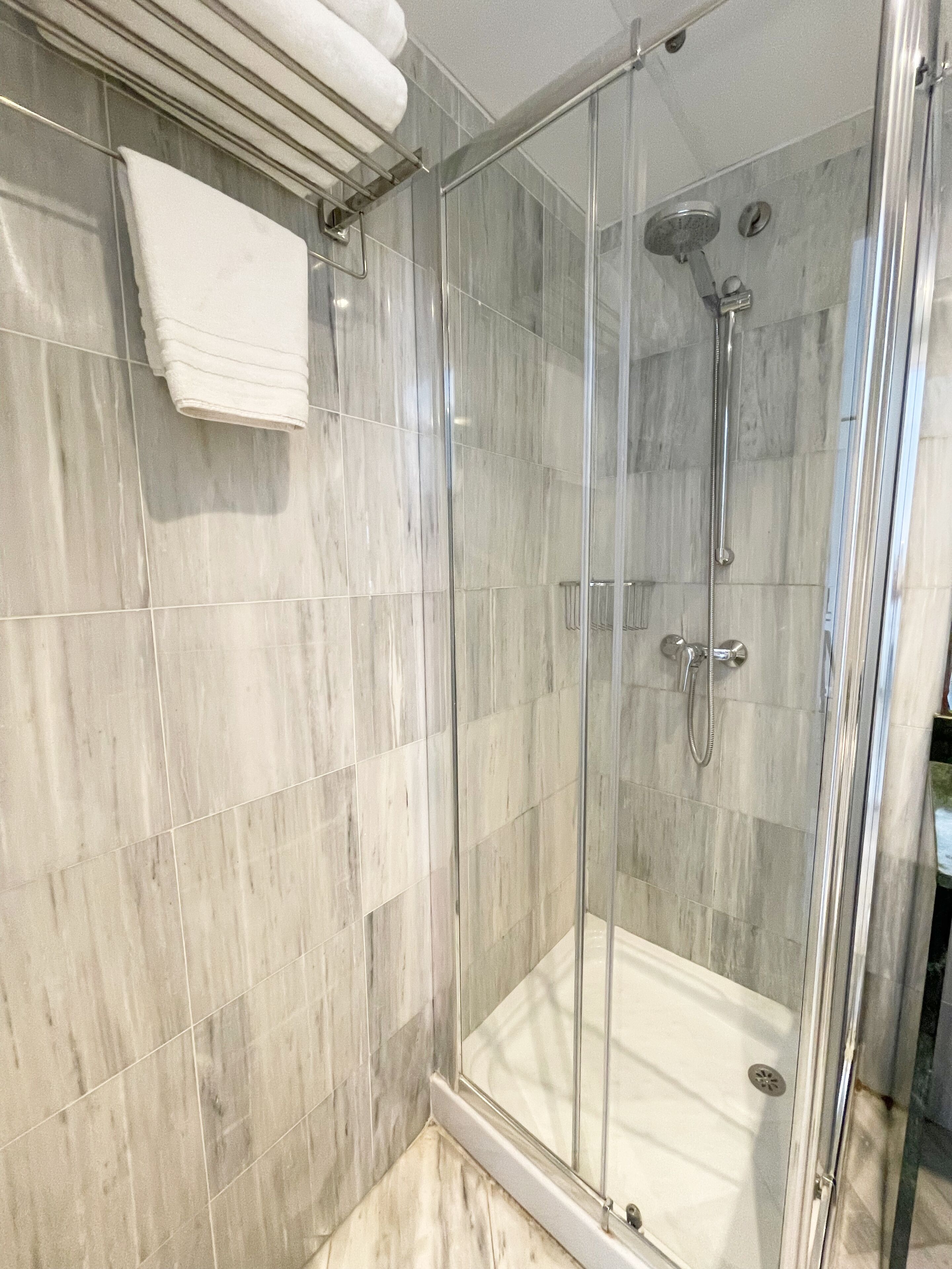 A glass-enclosed shower with a handheld showerhead and a wall-mounted faucet.