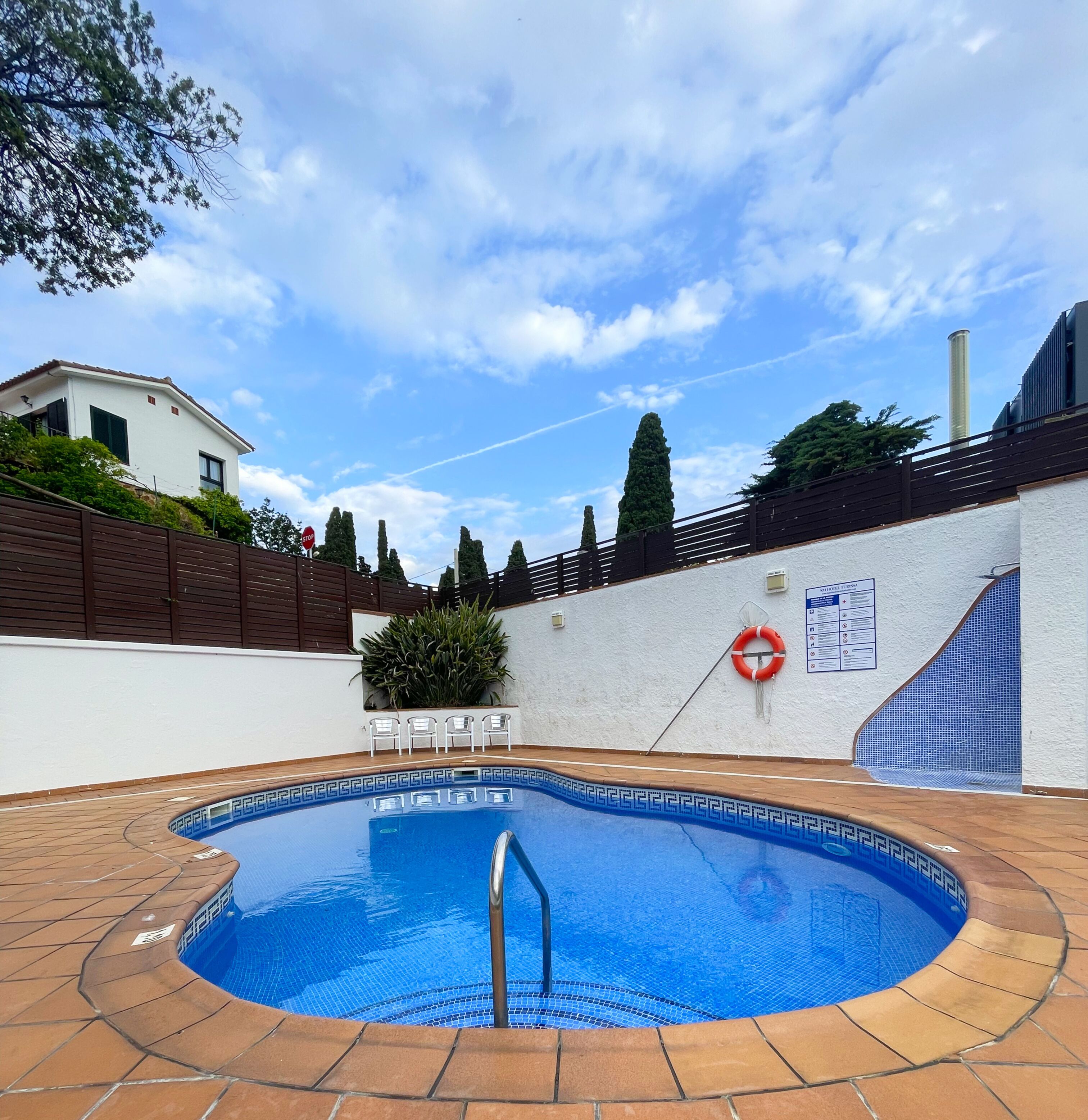 Una piscina con borde de azulejos, un flotador salvavidas y una señal de stop.