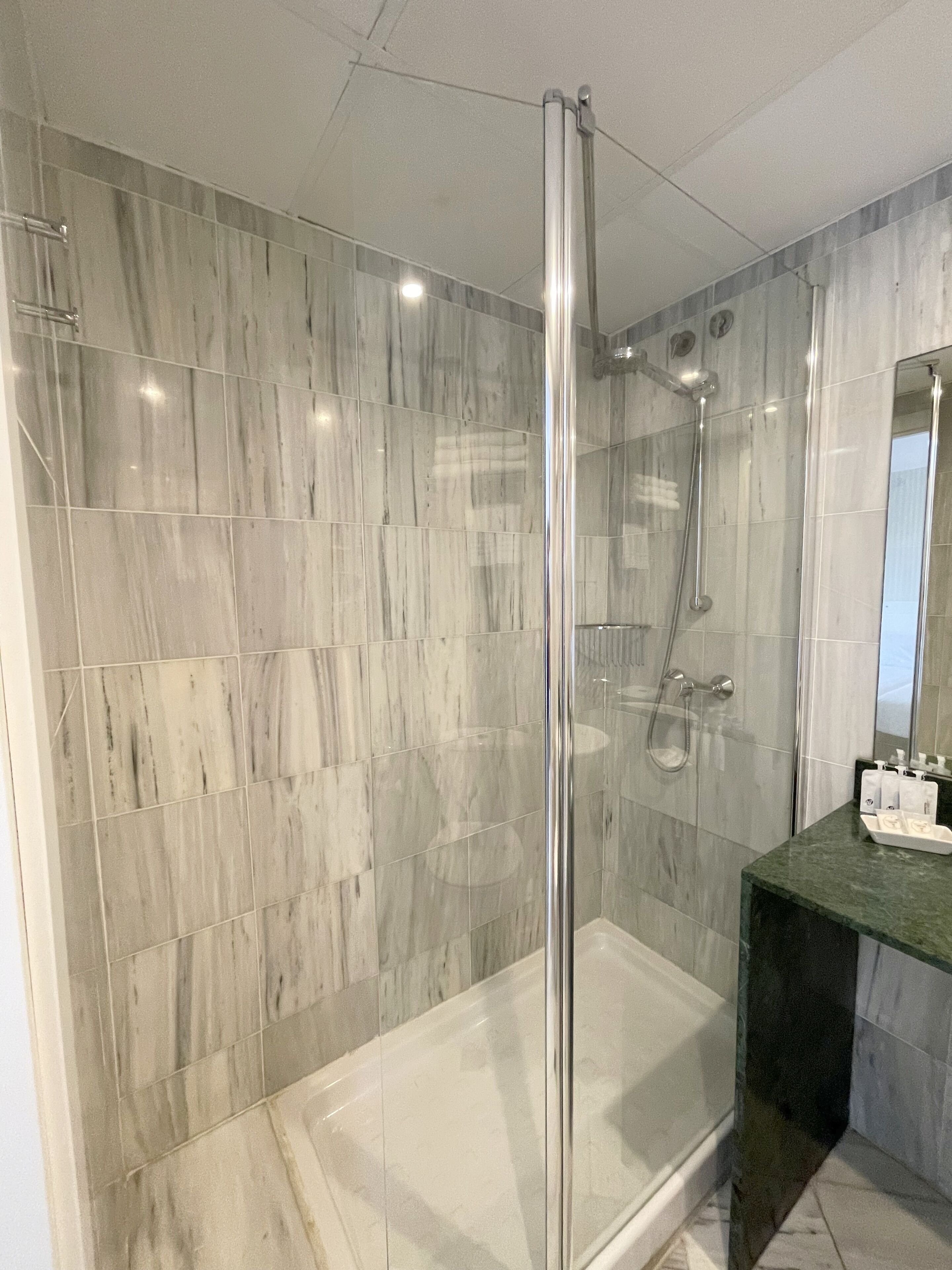 A modern bathroom with a glass-enclosed shower, marble tiles, and a green countertop.