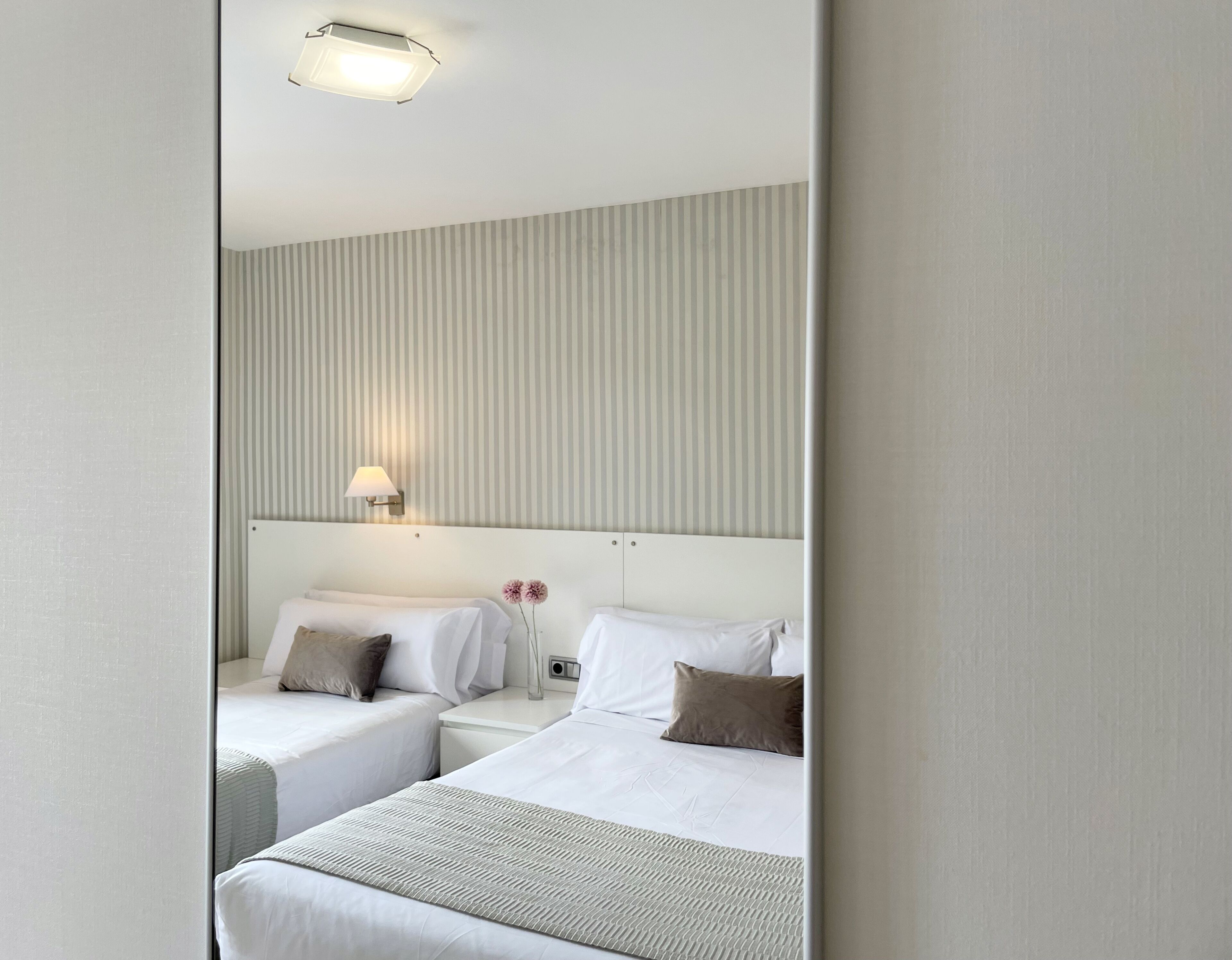 A hotel room with two beds, a headboard, a nightstand, a lamp, and a wall with vertical stripes.