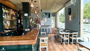 Un espace bar avec des comptoirs et des tabourets en bois, un téléviseur fixé au mur et un tableau affichant le menu.