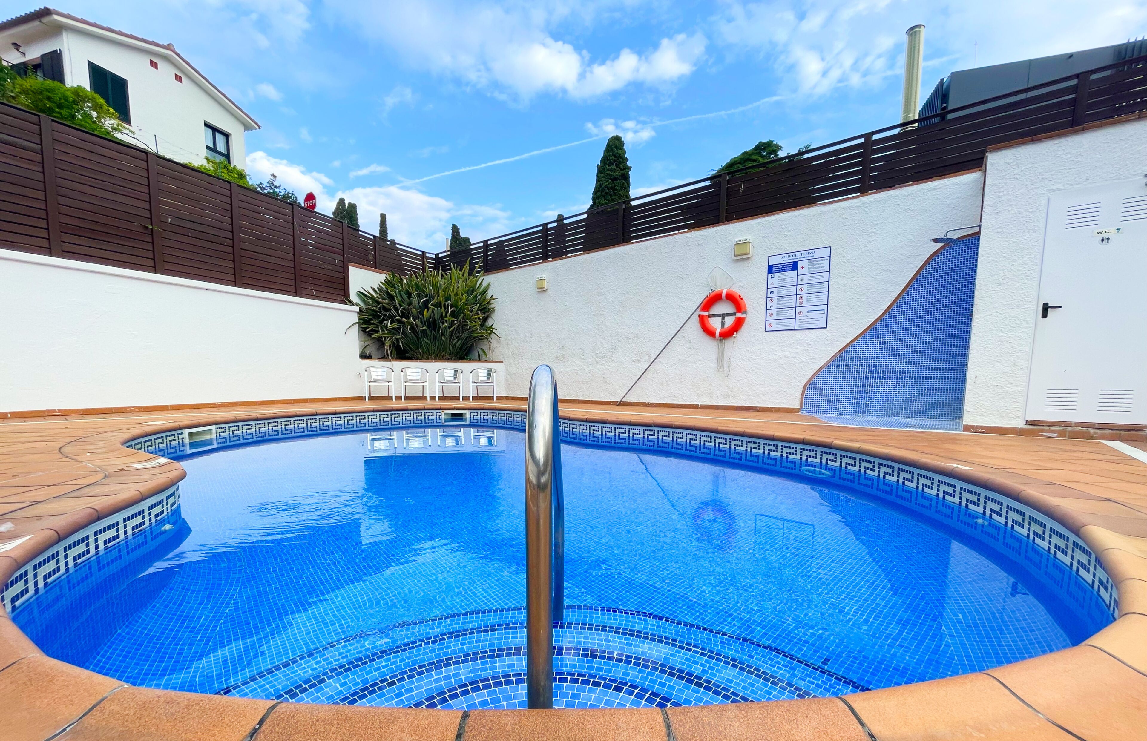 A swimming pool with a tiled edge, a lifebuoy, and a stop sign on a fence.