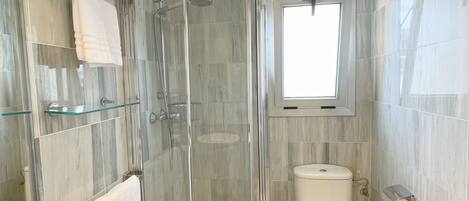A modern bathroom with a glass-enclosed shower, a toilet, and a sink with a marble countertop.