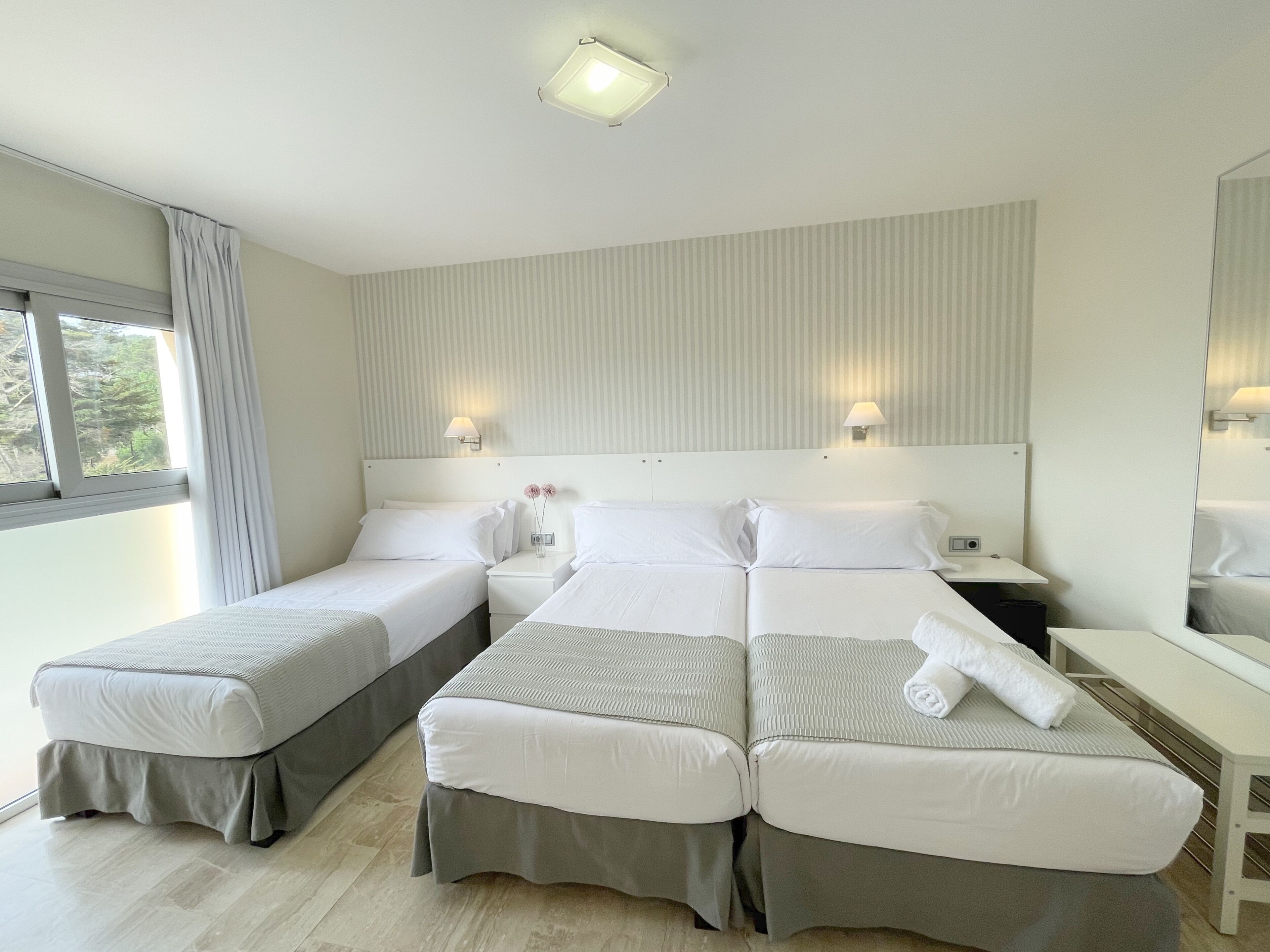 Une chambre d’hôtel avec deux lits, une table de chevet, une lampe et une fenêtre avec des rideaux.