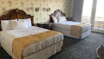 A hotel room with two beds, floral wallpaper, a wooden headboard, a small round table, and a balcony with a railing.