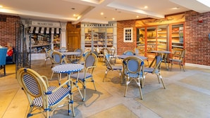 A cafe with wicker chairs and tables, a brick wall, and a bakery in the background.