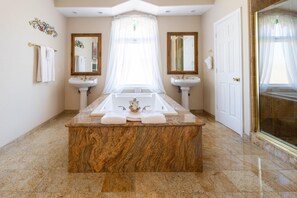 A bathroom with a marble bathtub, two sinks, and a shower area.