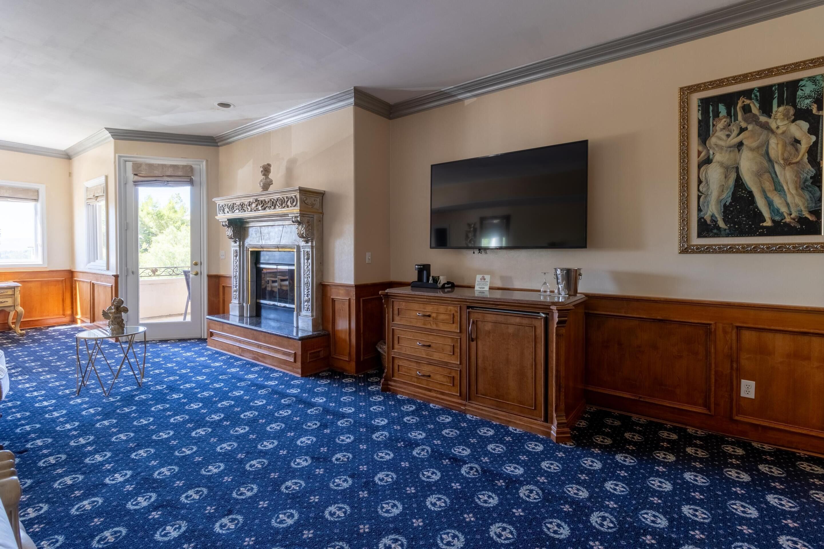 A room with a patterned carpet, a fireplace, a television, and a painting on the wall.