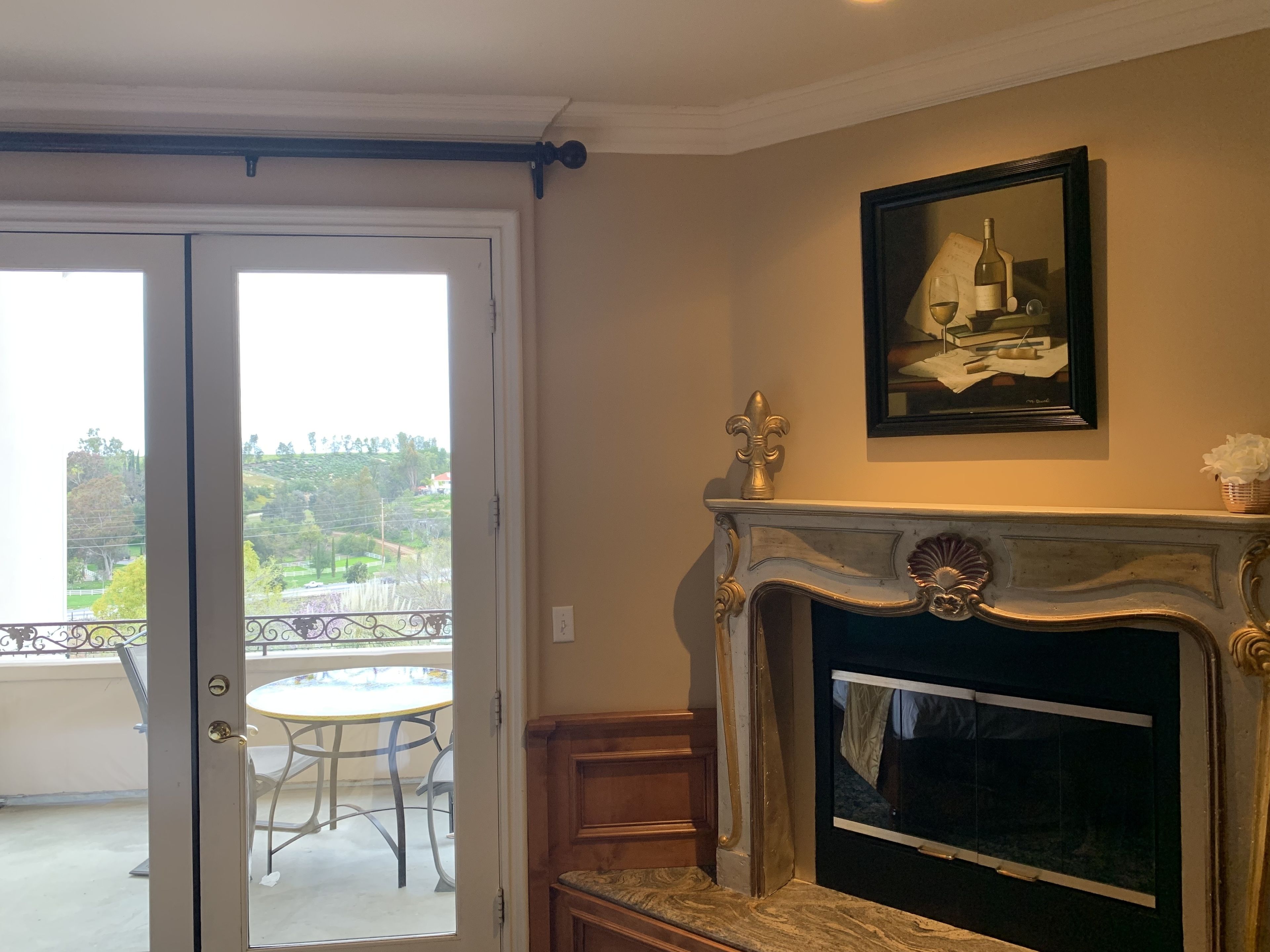 A room with a fireplace, a framed artwork above it, and a balcony with a table and chairs.