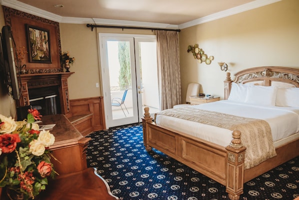A bedroom with a large bed, a fireplace, a desk, and a view of the outdoors.