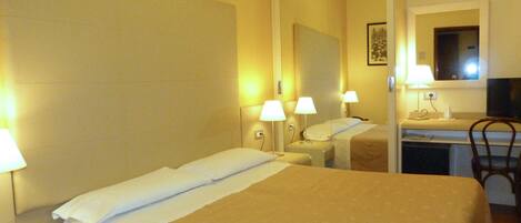 Habitación de hotel con dos camas, un escritorio y una silla. Hay lámparas en las mesitas de noche y un espejo sobre el escritorio.