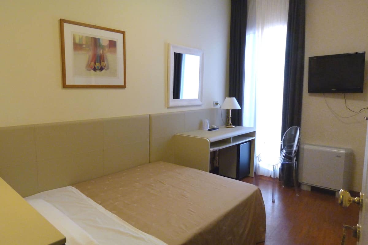 Ein Hotelzimmer mit Bett, Schreibtisch, Stuhl, Fernseher und einem Fenster mit Vorhängen.