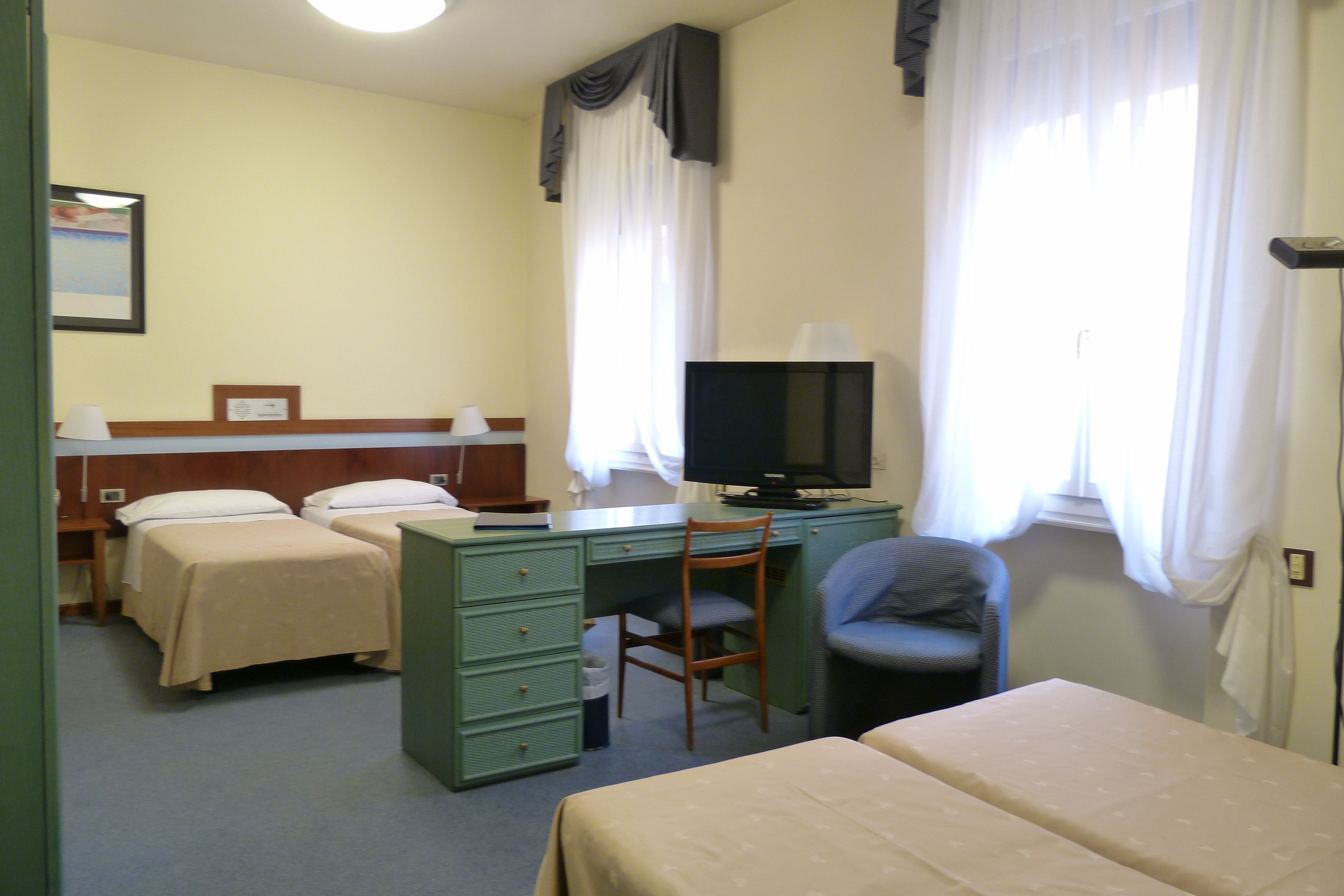 A hotel room with two beds, a desk with a chair, a television, and a window with curtains.