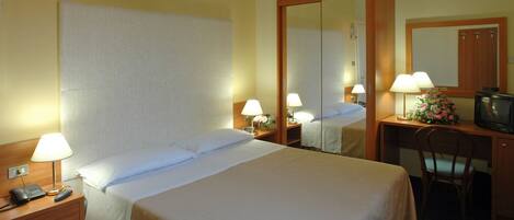 A hotel room with a large bed, bedside lamps, a desk with a television, and a mirror.