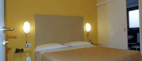 Habitación de hotel con cama, lámparas de noche, mesita de noche y baño a la vista a través de una puerta abierta.