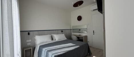 Un dormitorio con cama, escritorio, silla, espejo y televisor.