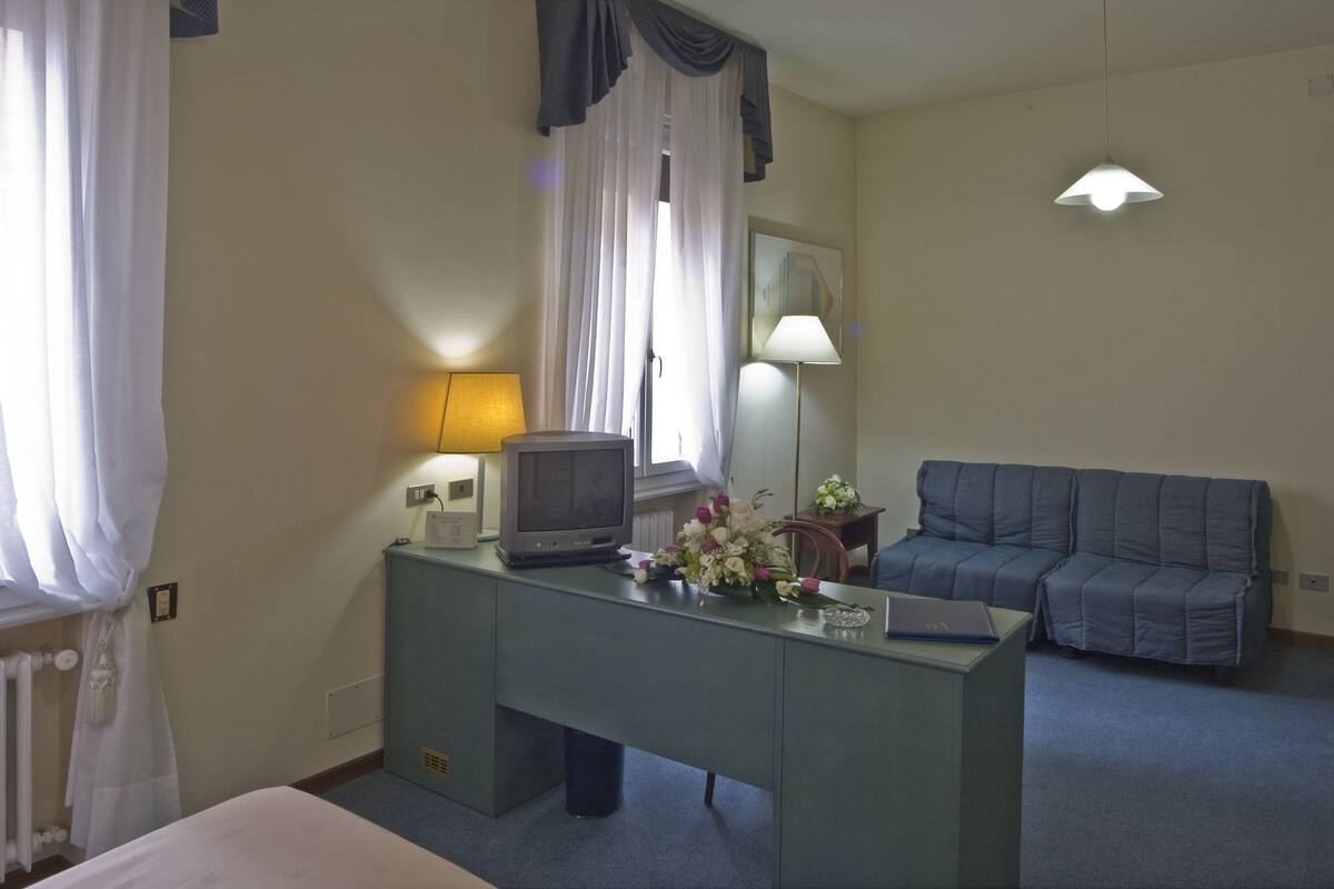 Ein Hotelzimmer mit einem Bett, einem Schreibtisch mit Fernseher, einem blauen Sofa und einer Lampe.