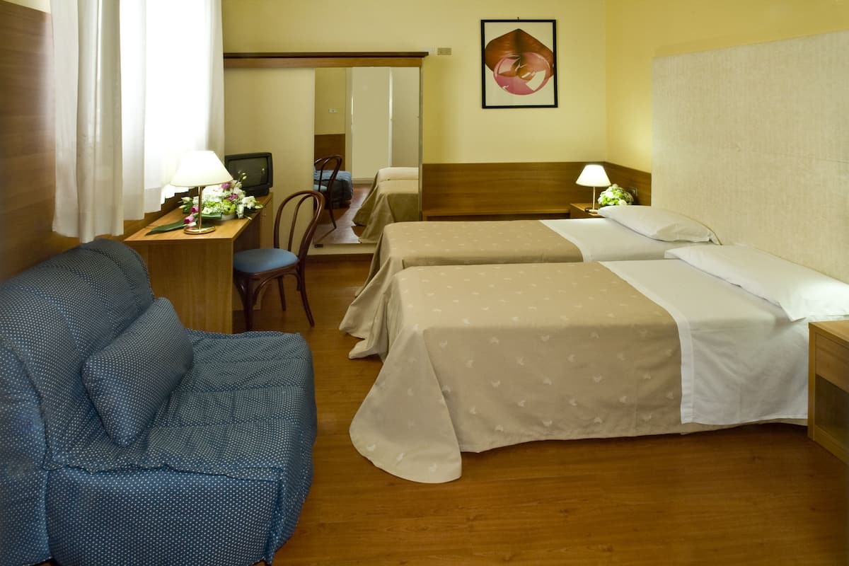 Ein Hotelzimmer mit zwei Betten, einem Schreibtisch mit Lampe, einem Sessel und einem Bett mit Blumen.