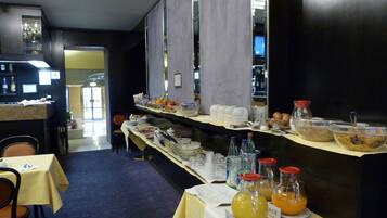 A buffet setup with various food items and beverages, including bowls of cereal and fruit juices, arranged on a counter with a yellow tablecloth.