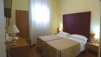 Une chambre d’hôtel avec deux lits, un bureau, une chaise, un miroir et une fenêtre avec des rideaux.