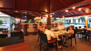 An indoor restaurant with wooden tables and chairs, a bar area, and a view of the outside.