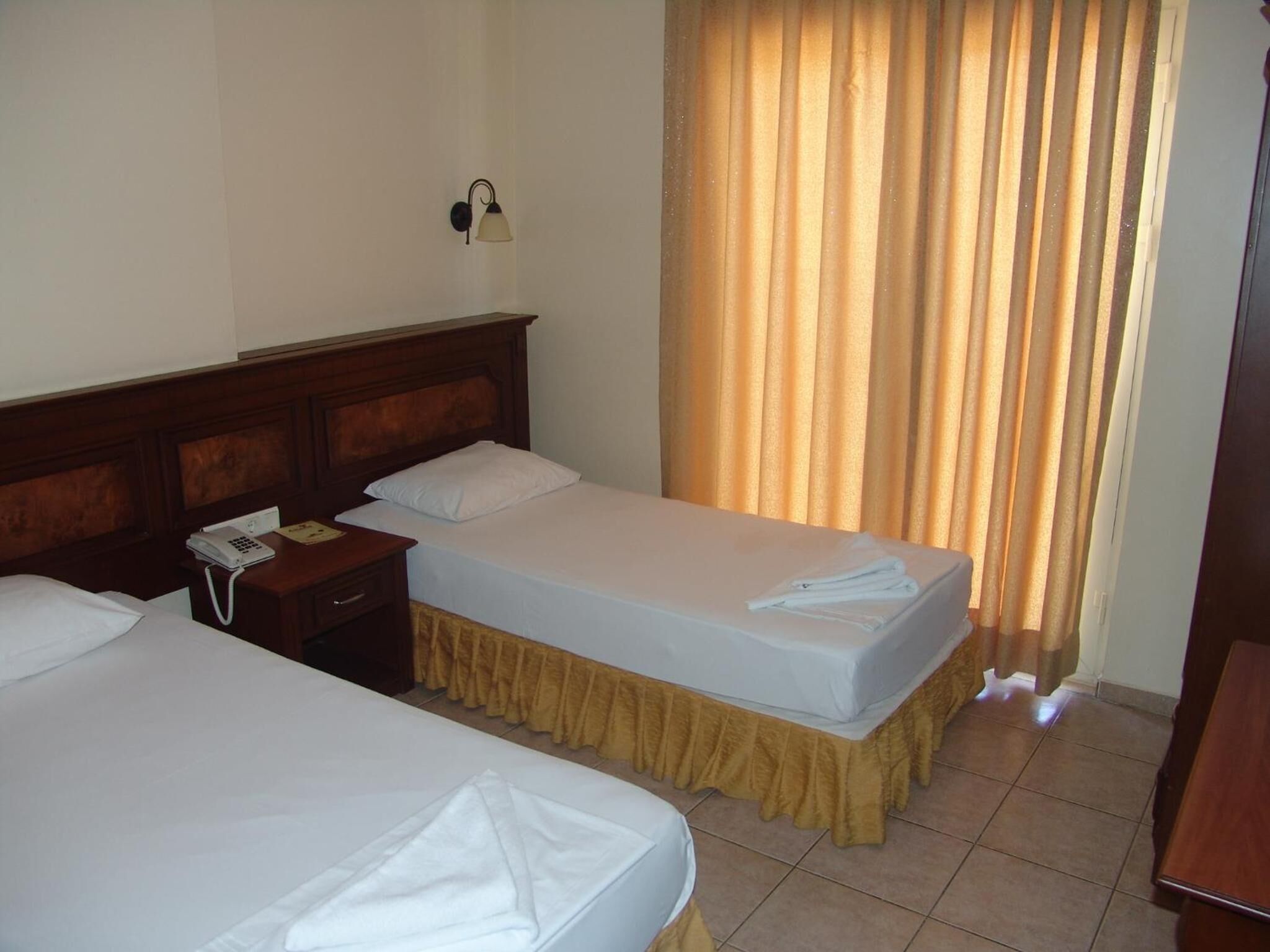 A hotel room with two beds, a bedside telephone, and a wall-mounted lamp.