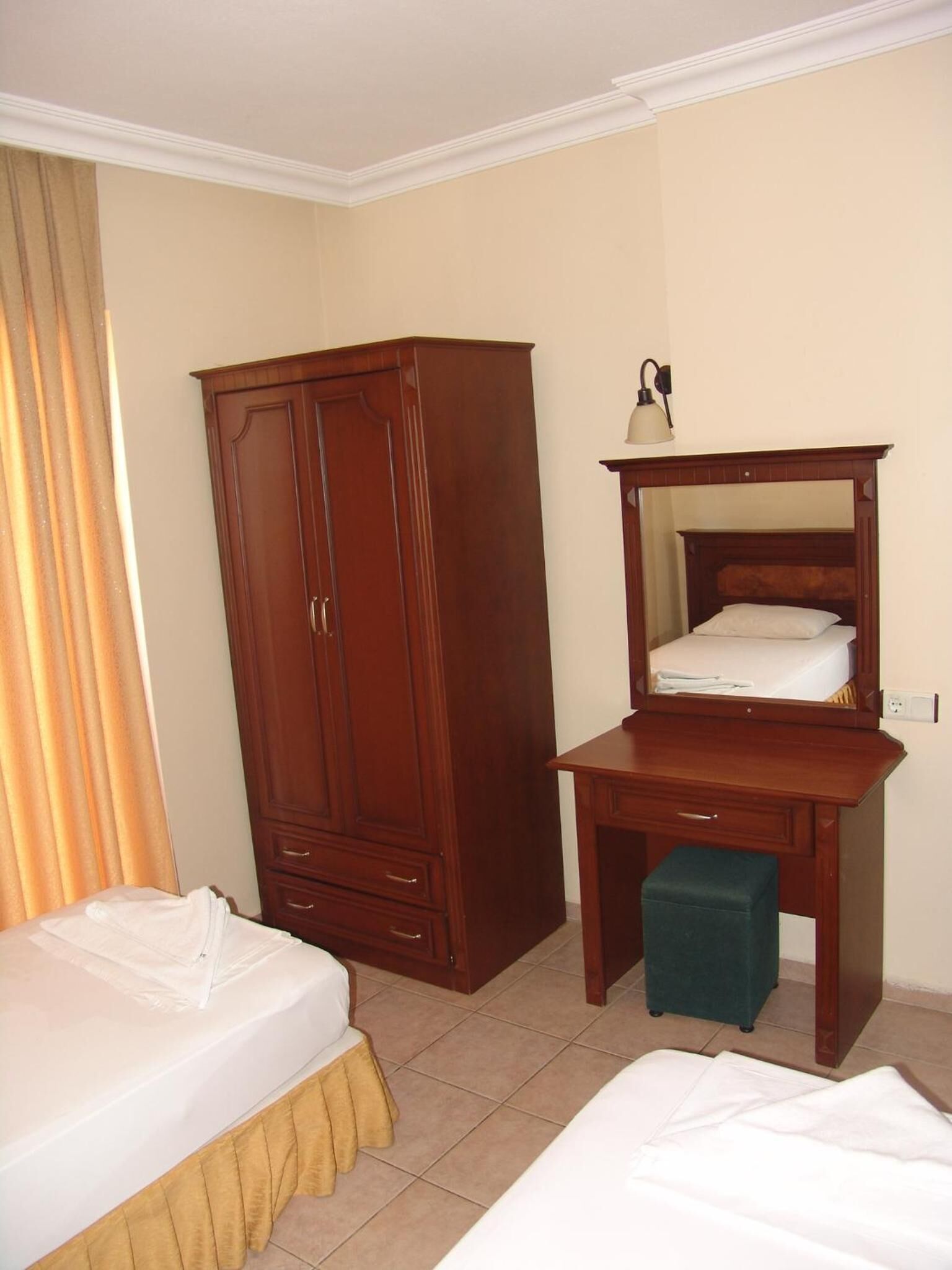 A hotel room with a wooden wardrobe, a desk with a mirror, and two beds.