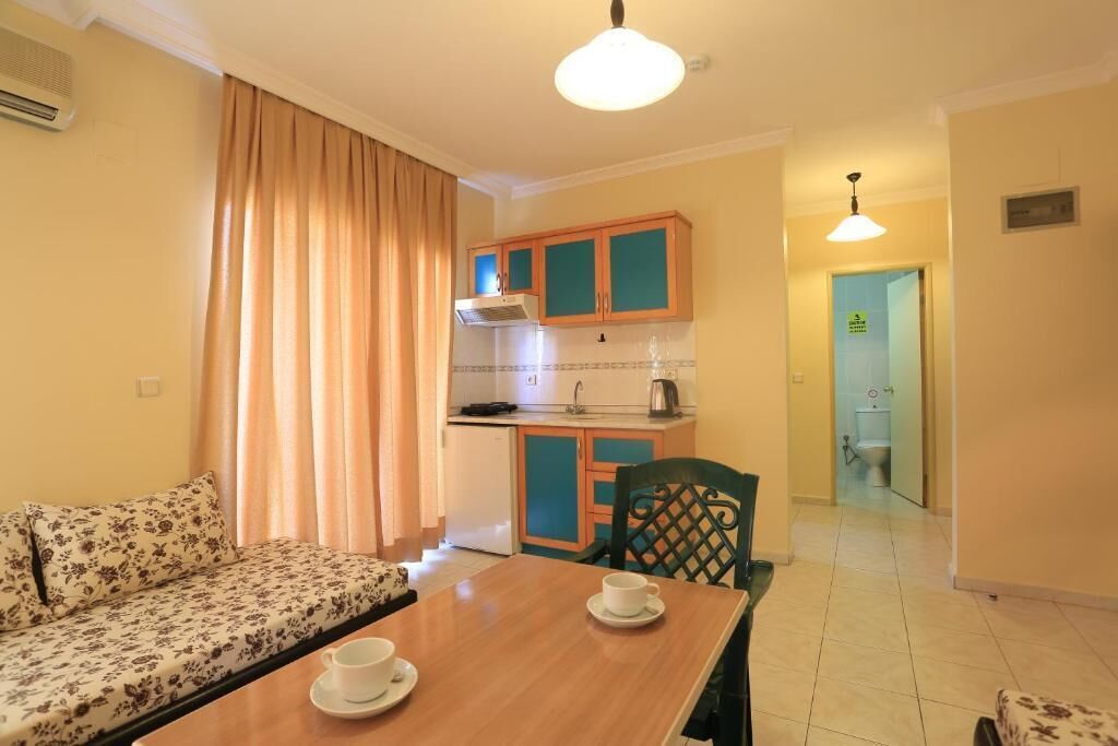 Un espace de vie compact comprenant un canapé, une table à manger avec deux tasses, une kitchenette avec des meubles de couleur turquoise et une salle de bain visible à travers une porte ouverte.