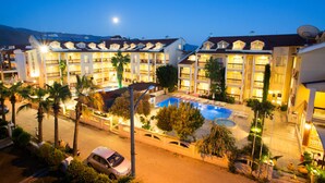 A hotel with multiple balconies, a swimming pool, and palm trees.