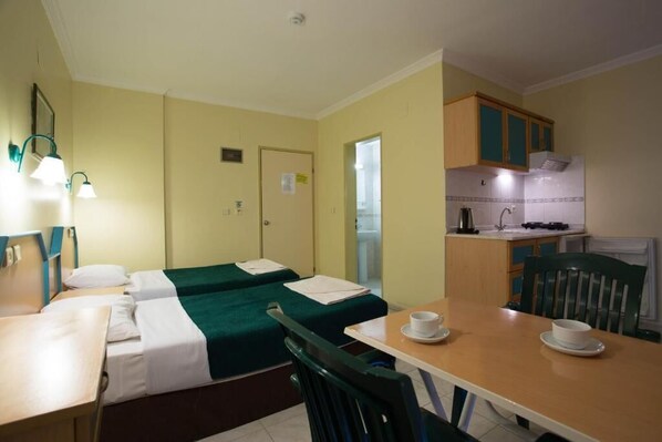 A hotel room with two single beds, a small kitchenette, a dining table with two chairs, and a bathroom visible through an open door. - Club Amaris Apartment (Marmaris)