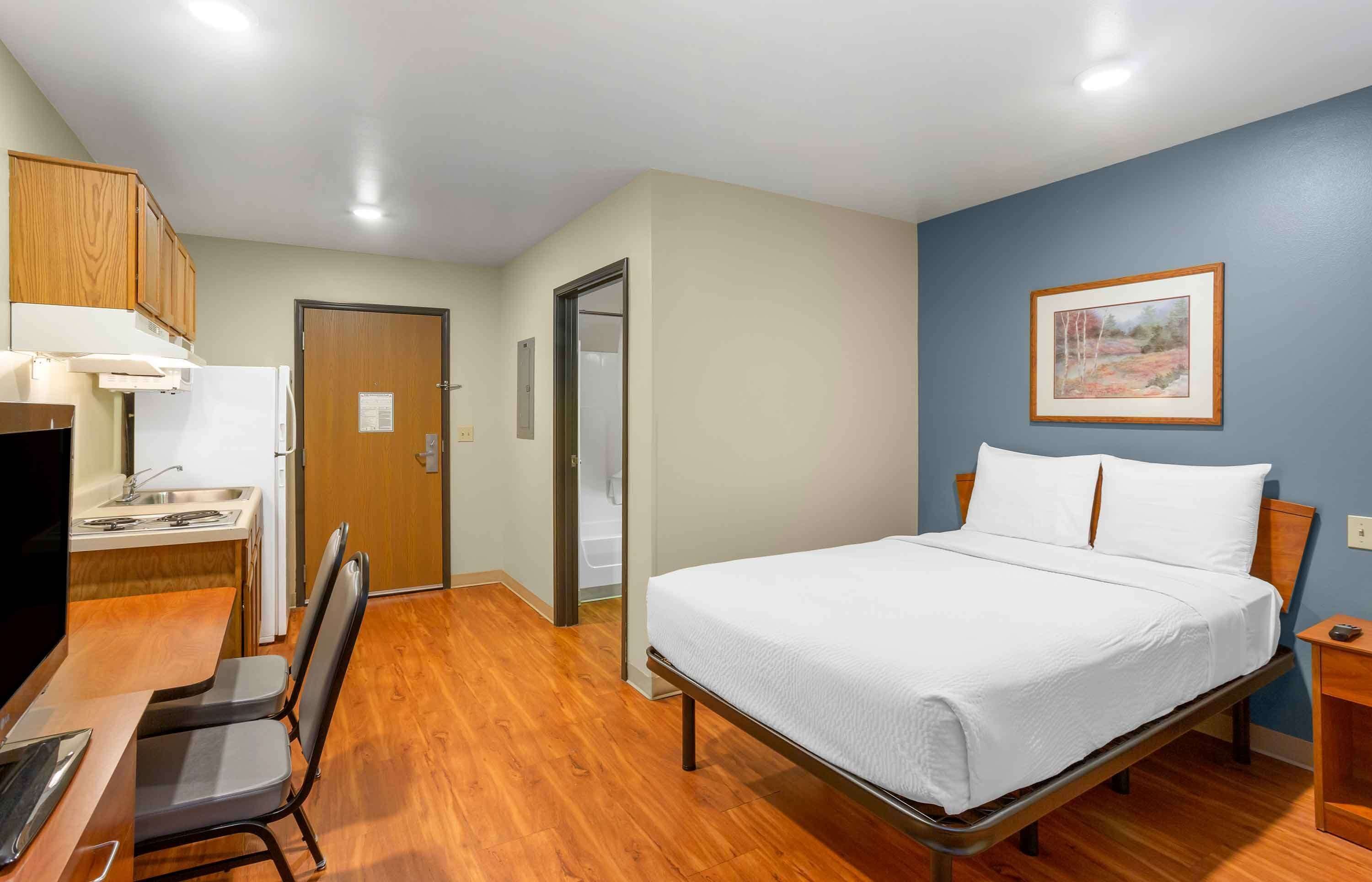 Un dormitorio con cama, escritorio, silla, kitchenette y baño.