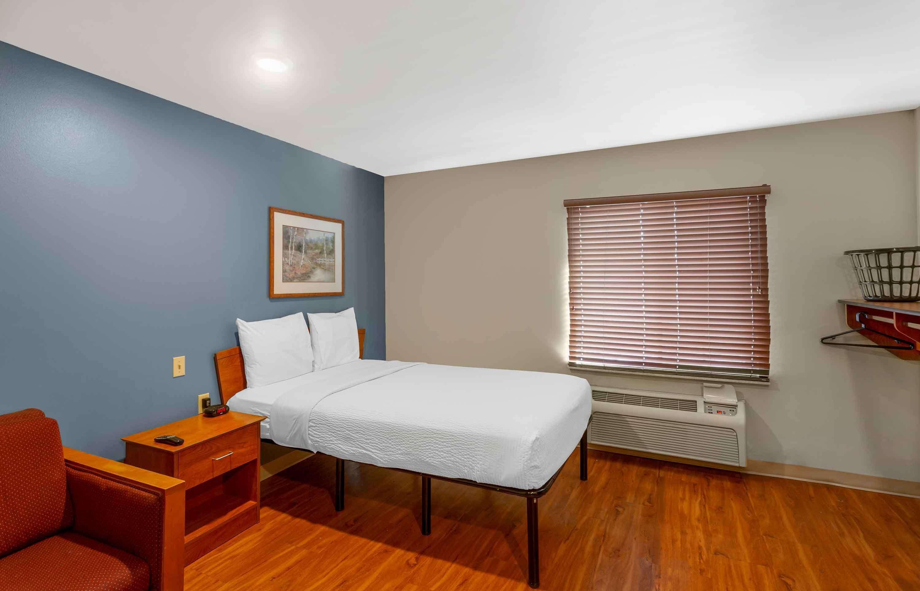 A bedroom with a bed, a desk, a chair, a picture on the wall, and a window with blinds.