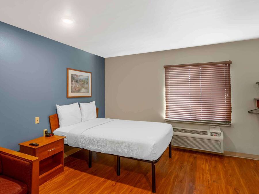 A bedroom with a bed, a desk, a chair, a picture on the wall, and a window with blinds.