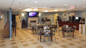 A dining area with tables and chairs, a fireplace, a television, and a kitchen counter with a refrigerator and coffee machine. - MainStay Suites Dover (Dover)