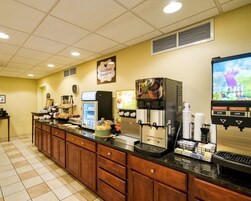 Un área de desayuno con cafetera, dispensador de fruta y vitrina refrigerada.