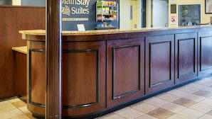 A MainStay Suites reception desk with a dark wood finish, a counter with a marble top, and a wall-mounted display of amenities. - MainStay Suites Dover (Dover)