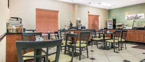 A clean, well-lit cafe with multiple tables and chairs, a coffee machine, and a refrigerator.