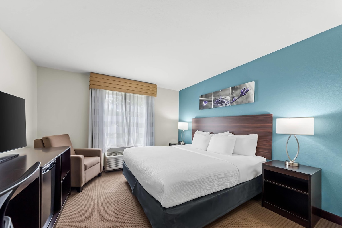 Habitación de hotel con cama, escritorio, silla, televisor y ventana con cortinas.
