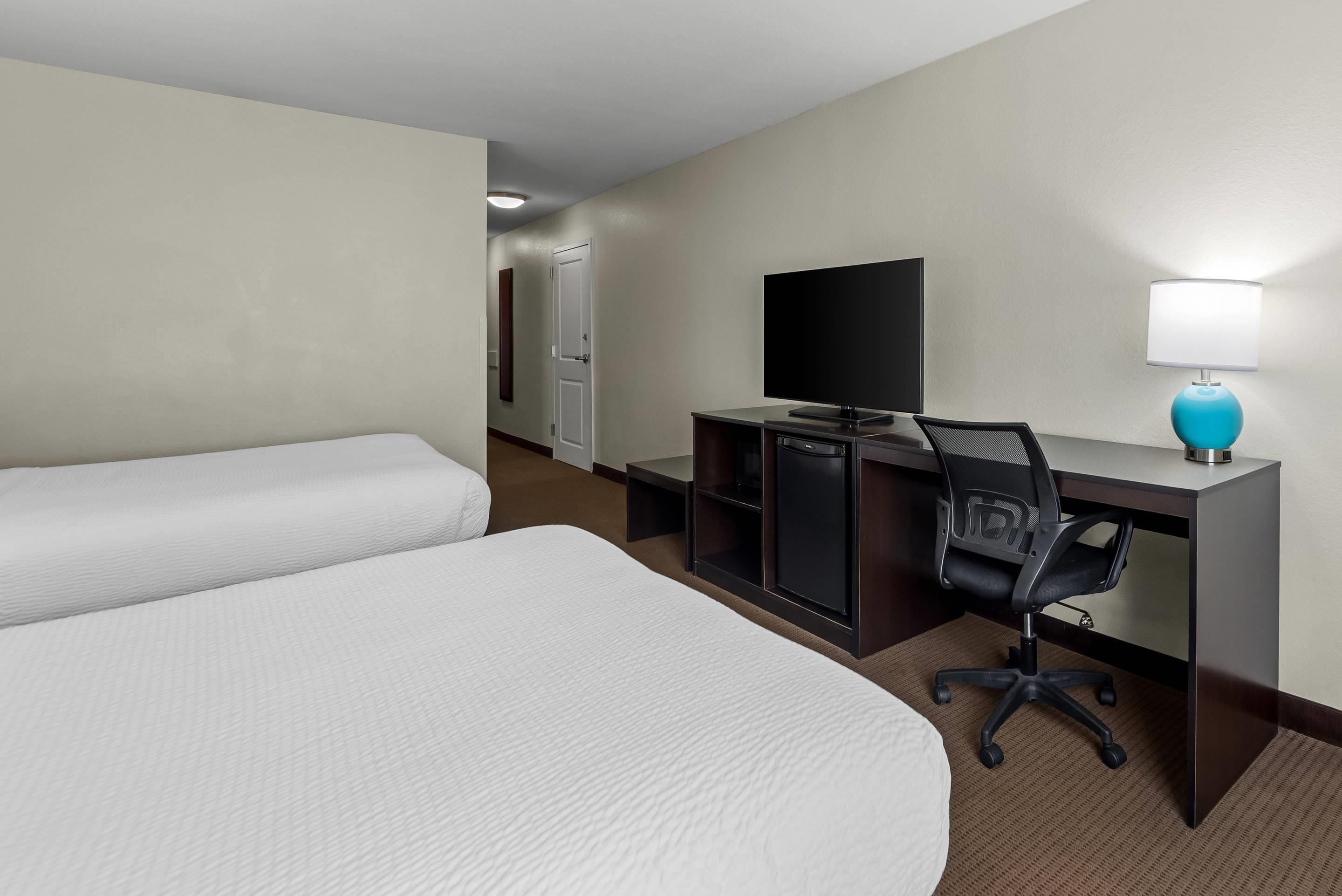 A hotel room with two beds, a desk with a television, a chair, and a lamp.