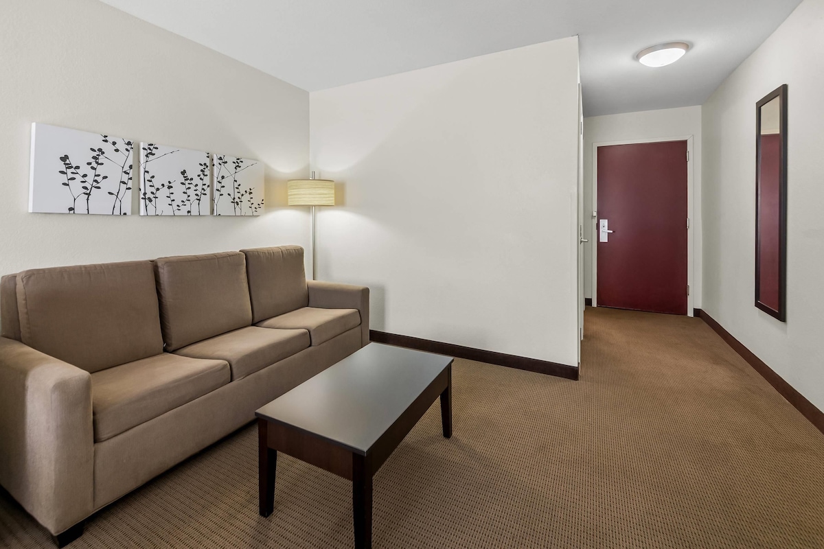 Una habitación de hotel con un sofá color beige, una mesita, una lámpara y una puerta que da a otra habitación.