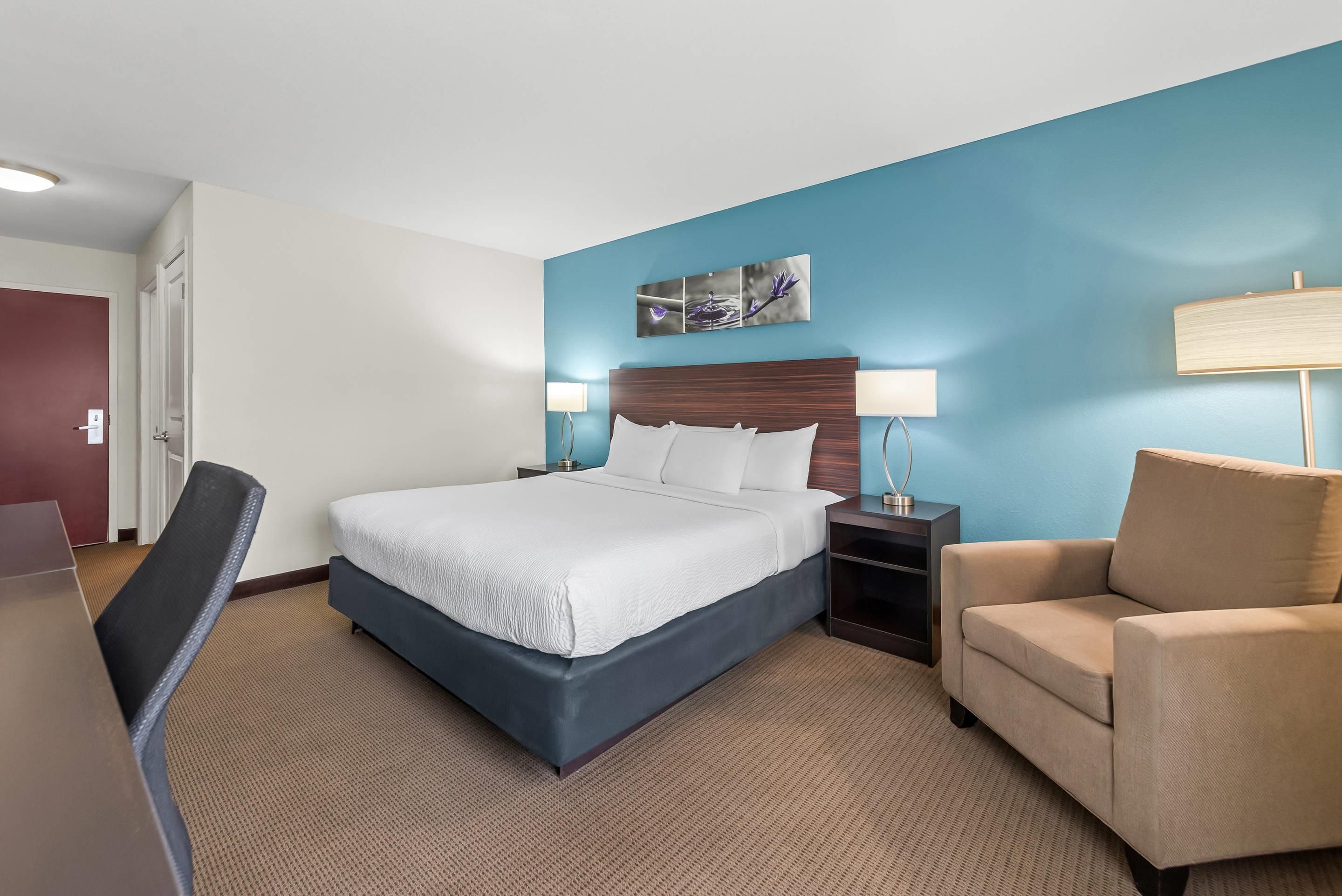 A hotel room with a bed, bedside tables, a chair, a desk, and a door.