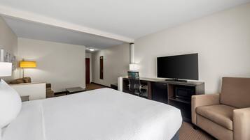 Una habitación de hotel con cama, escritorio, televisor, silla y lámpara.