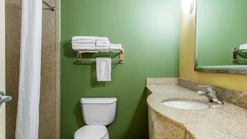 A bathroom with a green wall, a white toilet, a sink with a granite countertop, and a towel rack with folded towels.