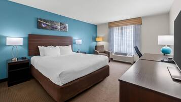 Een hotelkamer met een groot bed, nachtkastjes, een bureau, een stoel, een raam met gordijnen en een kunstwerk aan de muur.
