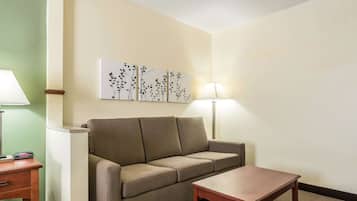 Une chambre d’hôtel avec un canapé beige, une table en bois et deux lampes fixées au mur.